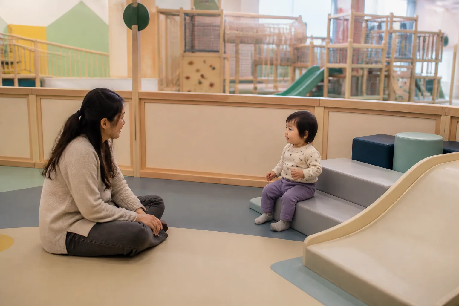 Caregiver beside a toddler in a low soft-play area.