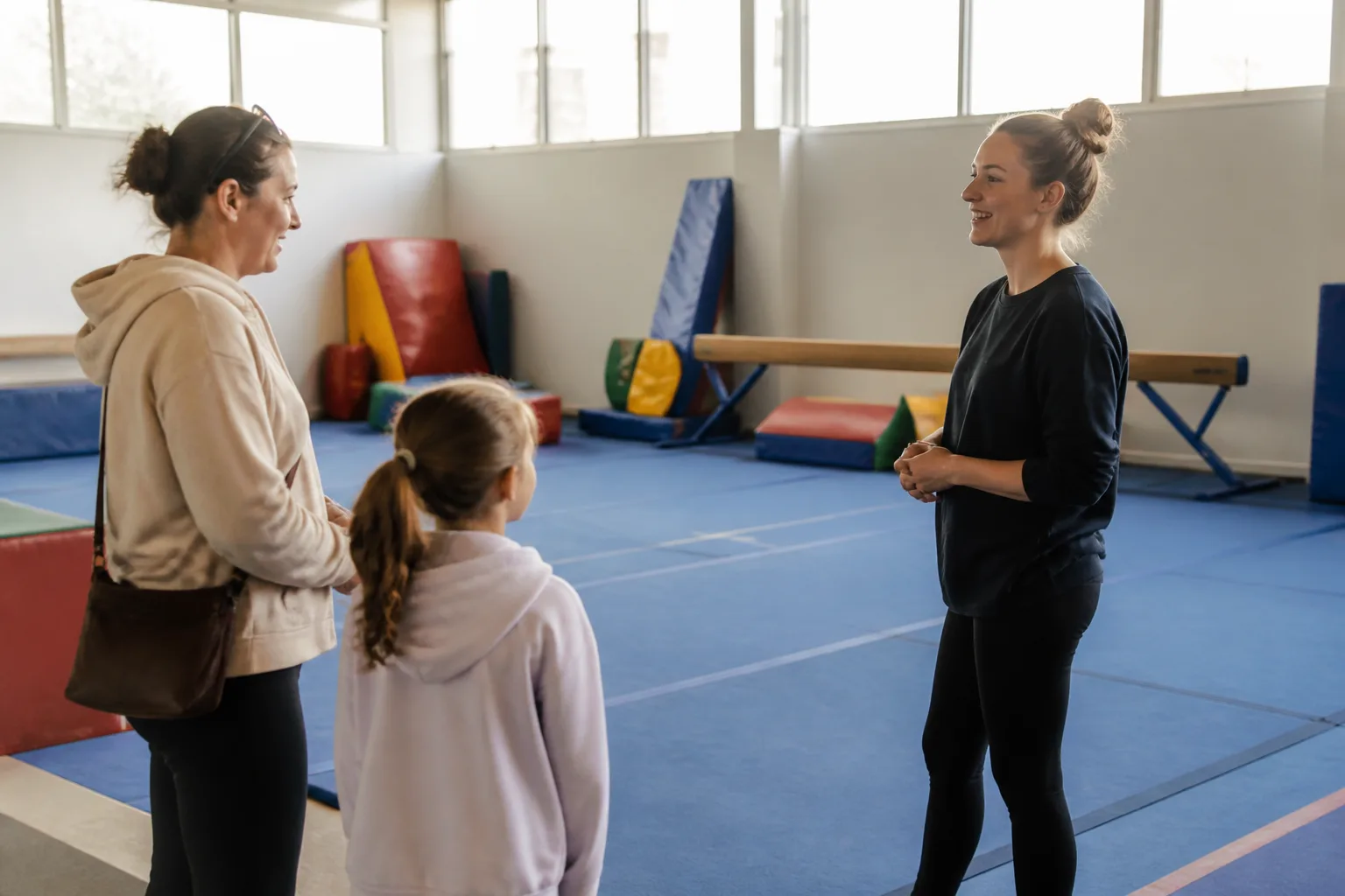 Child and caregiver speaking with a gymnastics coach before class.