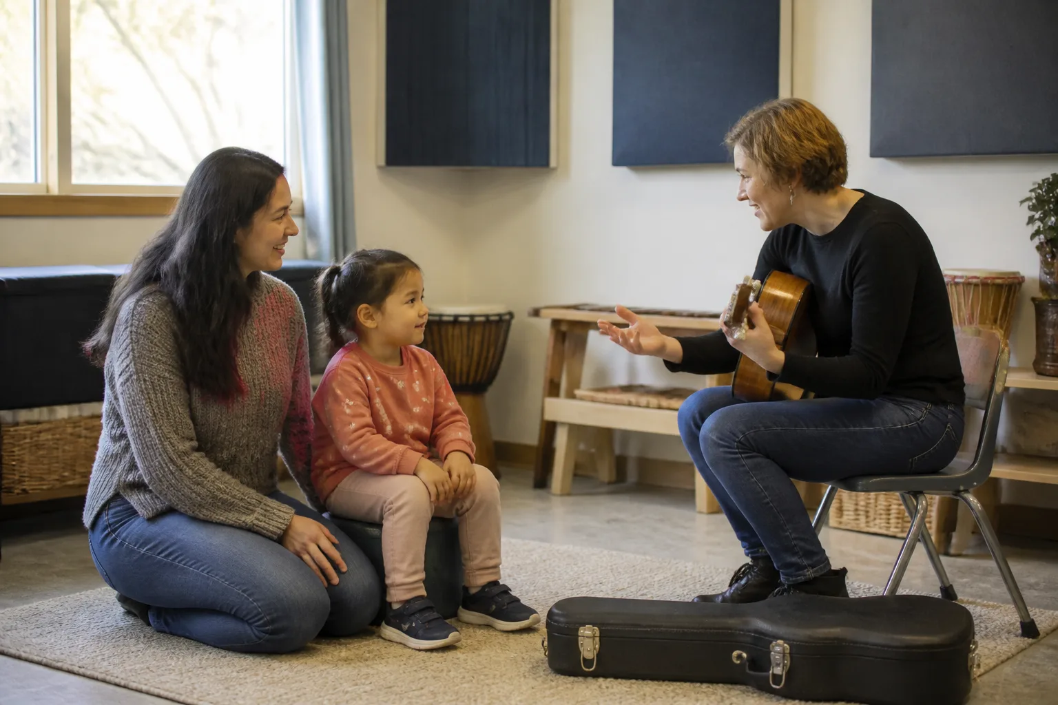 A guitar teacher plays for a seated parent and child.