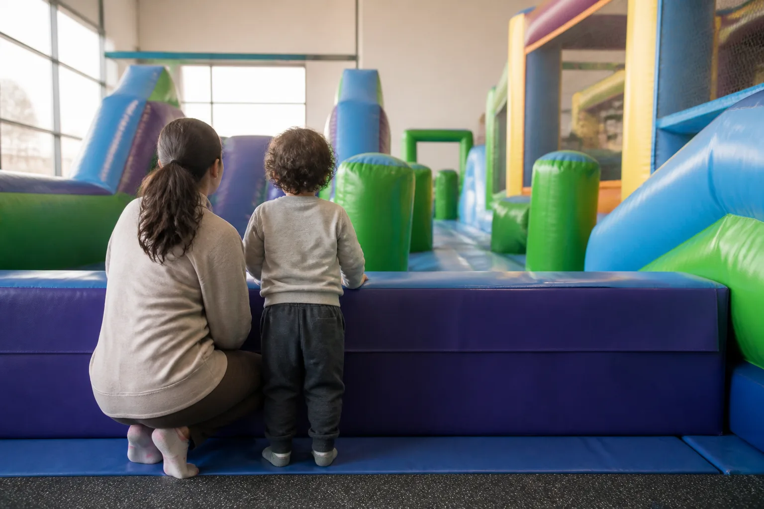 A parent and child look across a colourful padded inflatable play area.