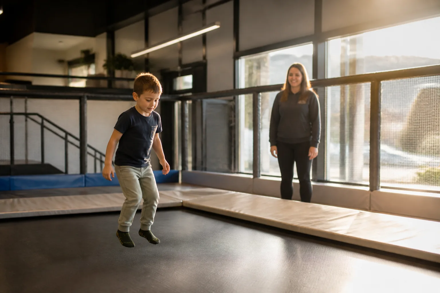 A child makes a small jump on a trampoline while an adult watches.