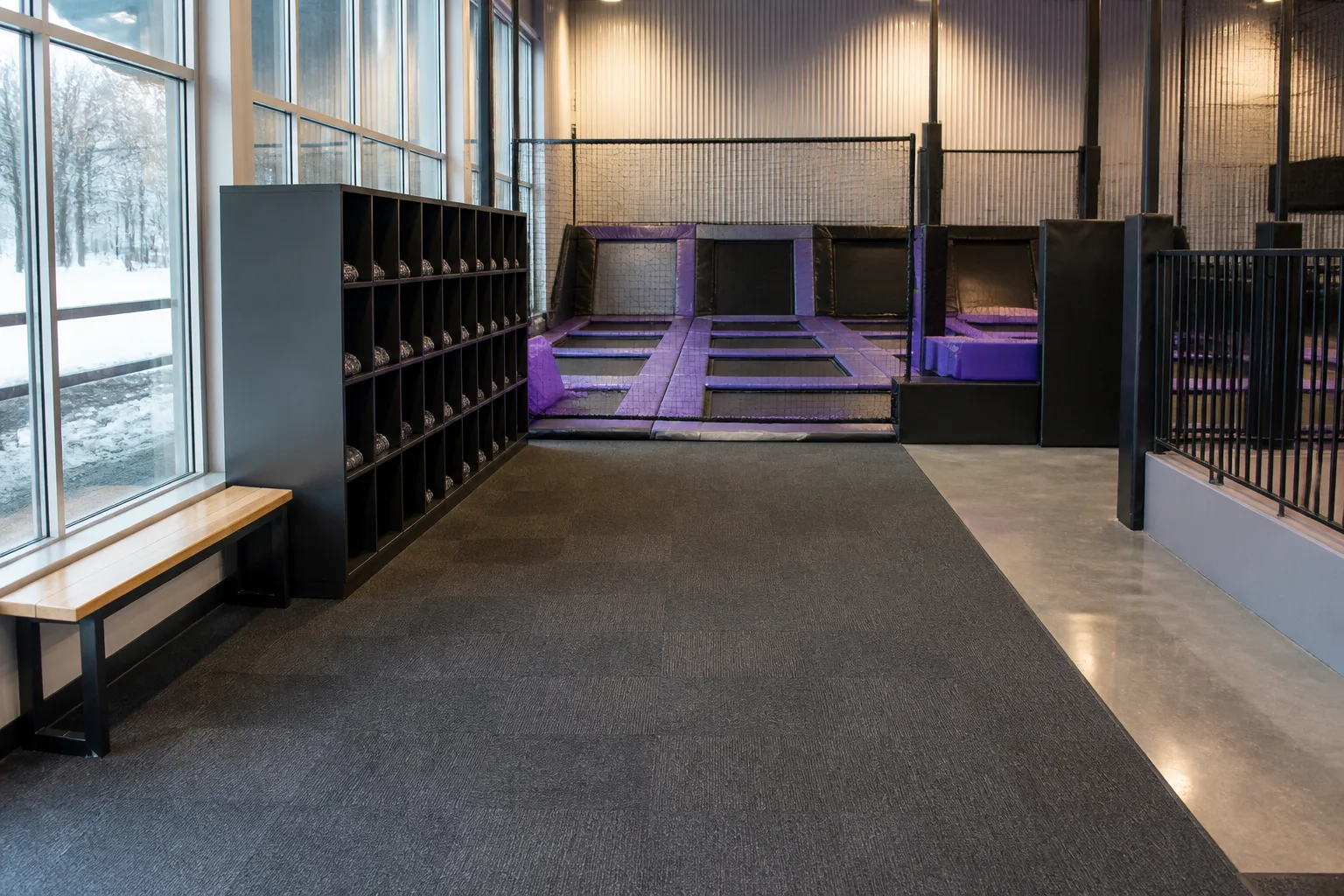 An empty trampoline area has a wide level walkway and black safety railings.