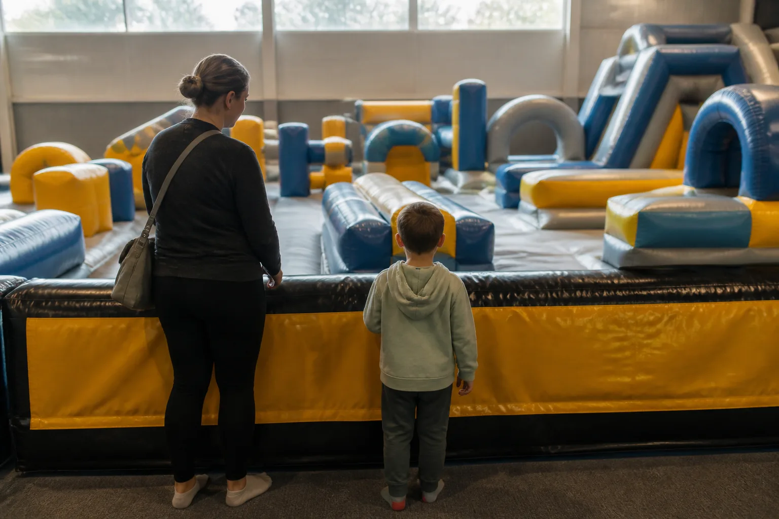 A parent and child stand beside a low padded inflatable attraction.
