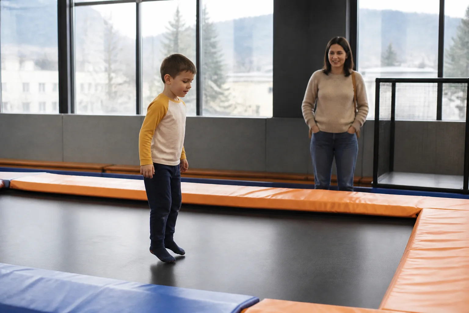 A child bounces on a trampoline while an adult supervises nearby.