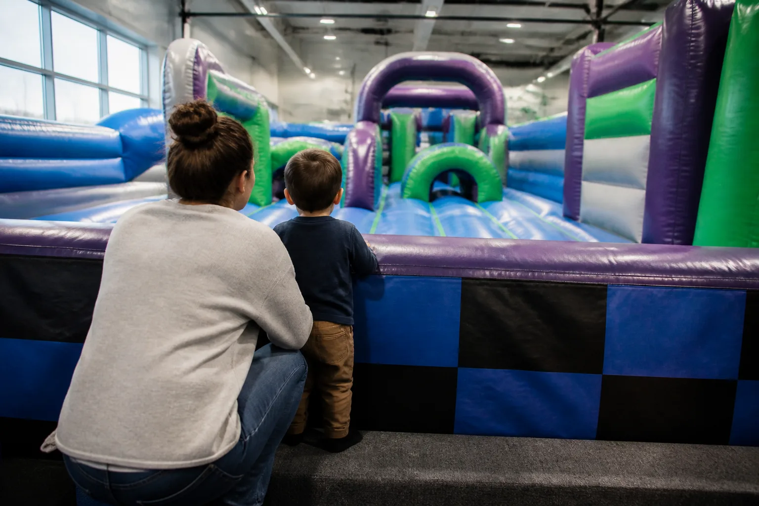 A parent and child watch a large indoor inflatable course.