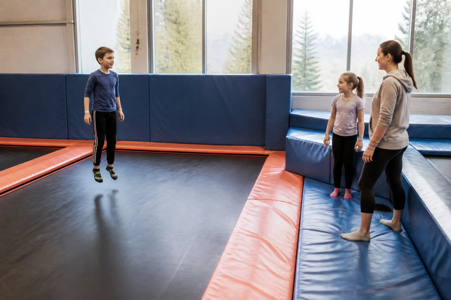 A parent and two children stand together on a padded trampoline lane.